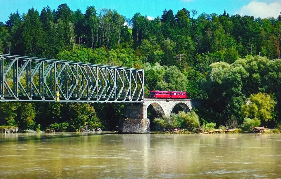 Vor einer Waldkulisse fährt ein roter Schienenbus auf die Kräutlsteinbrücke übr die Donau.