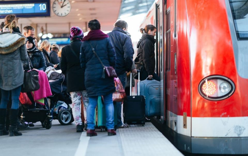 Menschen mit Gepäck stehen auf einem vollen Bahnsteig neben einem roten Zug im Bahnhof Köln Hbf