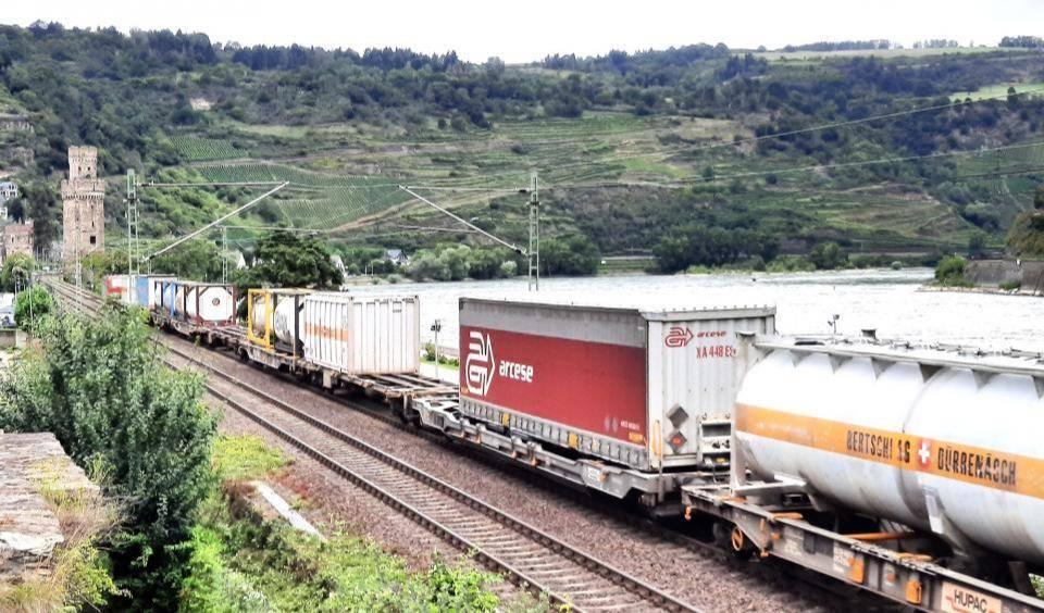 Güterzug mit Containern und Wechselaufbauten fährt am Rhein entlang