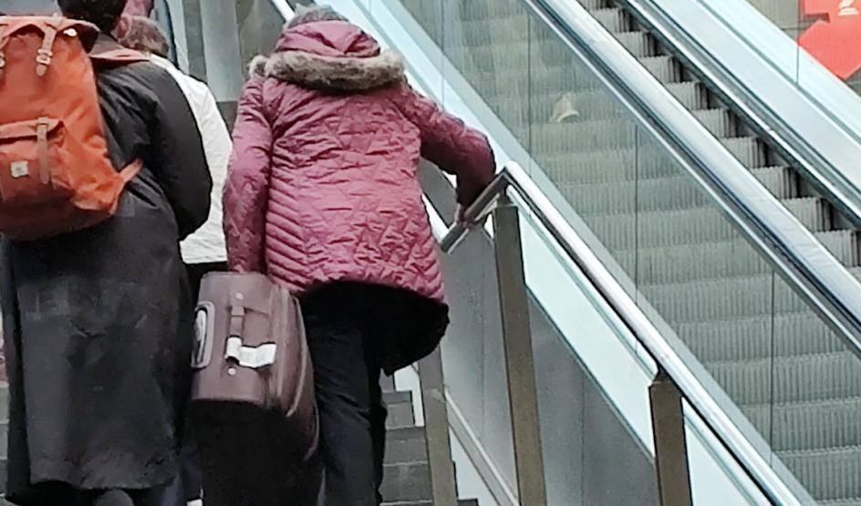 Menschen steigen eine Treppe neben einer stillstehenden Rolltreppe in einem Bahnhof hinauf