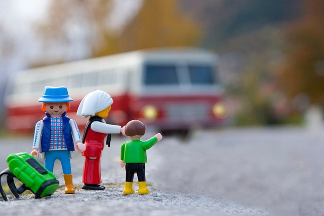 3 Playmobil-Figuren stehen am Straßenrand. Im Hintergrund, sehr unscharf, fährt ein Bus auf sie zu.